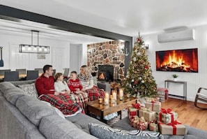A cozy living room with a fireplace, a Christmas tree, and a sofa with people sitting on it.