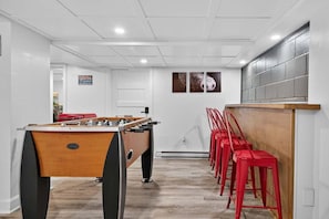 A room with a foosball table, red bar stools, and a wall-mounted TV.