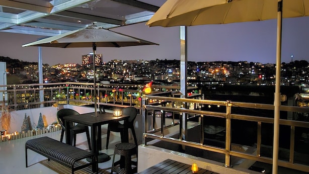 Een balkon met een tafel en stoelen, een leuning, en een uitzicht op een stadsbeeld bij nacht.
