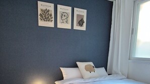 Een slaapkamer met een bed, een nachtkastje met een lamp, en drie ingelijste kunstwerken aan de muur.
