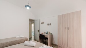 Une chambre avec deux lits, un bureau, une armoire et un luminaire suspendu.