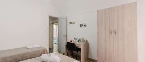 A bedroom with two beds, a desk, a wardrobe, and a hanging light fixture.