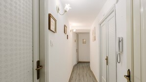 Un couloir avec un papier peint à motifs, un luminaire, des tableaux encadrés et une porte avec un téléphone.