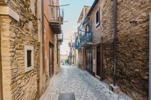 Une ruelle étroite, pavée de pierres, située entre des immeubles dotés de balcons, et fermée par une grille métallique à son extrémité.