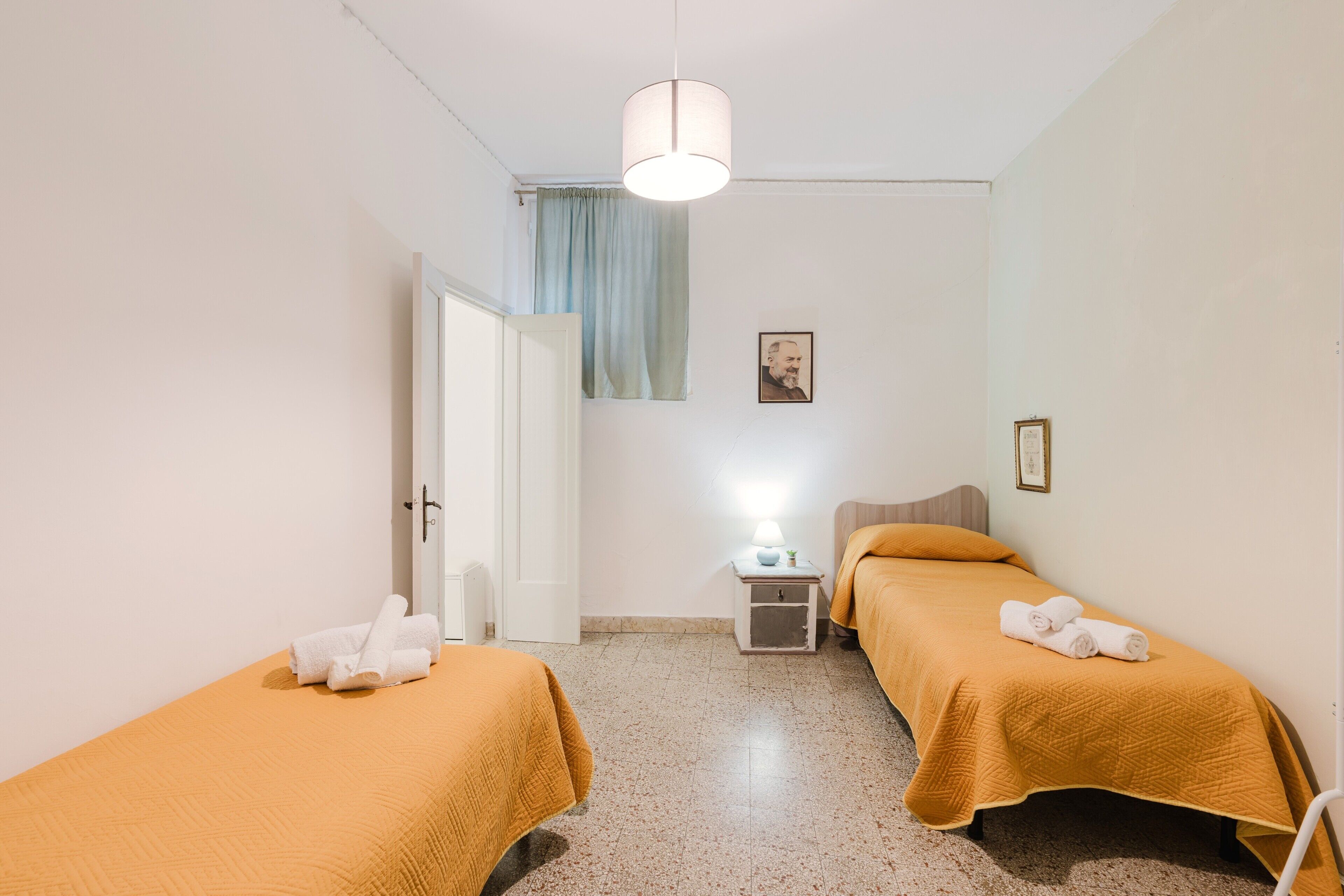 Une chambre avec deux lits, une table de chevet, une lampe et une porte.