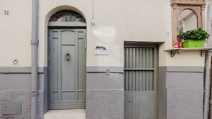 Un immeuble dont les portes sont numérotées, un petit balcon orné d’un pot de fleurs et un coffret de raccordement électrique.