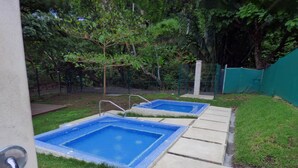 Two square swimming pools with blue tiles, surrounded by grass and trees, with a concrete deck in the foreground. - Ocean View Apt | Beach Club | Playa Mantas (Punta Leona)