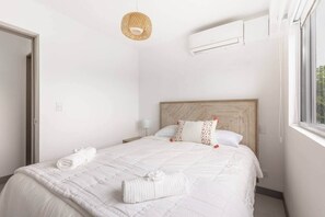 Un dormitorio con cama, lámpara colgante, equipo de aire acondicionado y ventana.