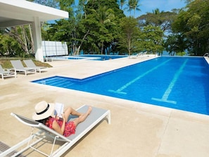 A swimming pool with lounge chairs and a person reading a book.