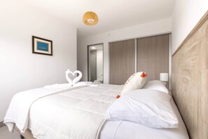 Et hotelværelse med seng, hvid sengetøj, et billed ophængt på væggen, et spejl og en træsenggavl.