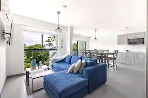A modern living room with a blue sofa, a dining area, and a kitchen.