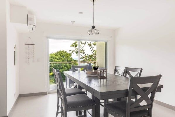 A dining area with a table and chairs, a hanging light fixture, and a view of greenery outside. - Ocean View Apt | Beach Club | Playa Mantas (Punta Leona)