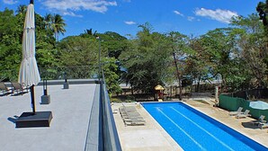 A rooftop pool with lounge chairs and umbrellas, surrounded by trees and a clear sky. - Ocean View Apt | Beach Club | Playa Mantas (Punta Leona)
