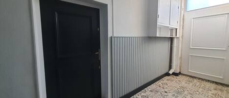 A hallway with a black door, white walls, a radiator, and patterned floor tiles.