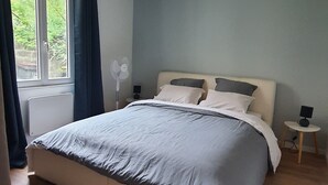 Une chambre à coucher avec un grand lit, un ventilateur de plafond, une fenêtre avec des rideaux et une table de chevet avec une lampe.