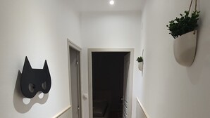 Un couloir doté d’un plancher en bois, de murs blancs et d’un luminaire au plafond.