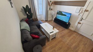 Un salon avec un canapé, une table basse, un téléviseur et une plante.