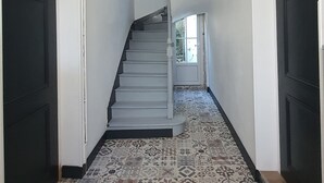 Un couloir avec un sol à motifs, un escalier et deux portes noires.