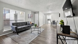 Ein modernes Wohnzimmer mit einem grauen Sofa, einem runden Couchtisch und einem an der Wand montierten Fernseher.