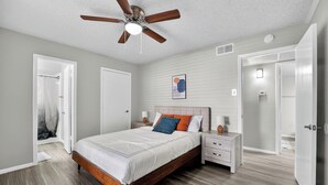 Ein Schlafzimmer mit einem hölzernen Bett, weißen Wänden, einem Deckenventilator und einem gerahmten Kunstwerk an der Wand.
