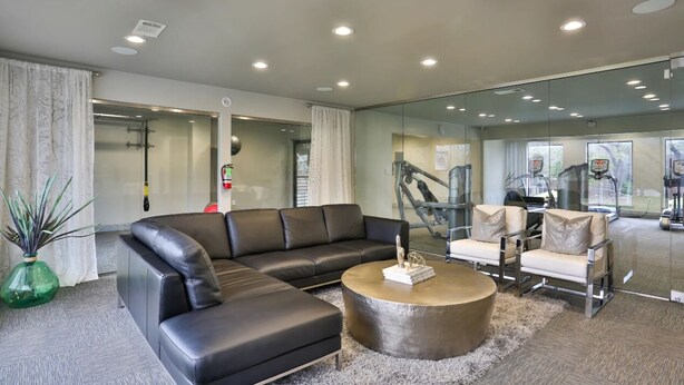 Eine moderne Lobby mit einer Ledersofa, einem runden Couchtisch und Glaswänden mit Blick auf das Fitnessstudio.