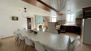 Un vaste espace de salle à manger avec une grande table et des chaises, une cuisine équipée d’appareils modernes et un luminaire décoratif au plafond.
