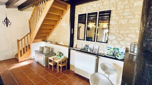 Une cuisine avec un escalier en bois, un mur en pierre et un plan de travail sur lequel sont disposés divers objets.