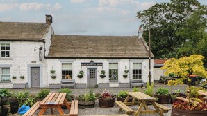 A white building with a sign reading "BLACKSMITHS ARMS". There are outdoor wooden benches and potted plants in front. - Daleholme (Barnard Castle)