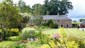 A stone building with a well-maintained lawn and various flowering plants. - Cosy Cottage set in lovely gardens, 2 miles east of the seaside town of Nairn (Auldearn)