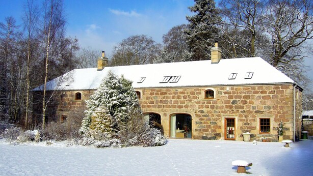 A stone building with a snow-covered roof, multiple windows, and a chimney. - Cosy Cottage set in lovely gardens, 2 miles east of the seaside town of Nairn (Auldearn)