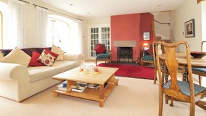 A living room with a sofa, coffee table, fireplace, and dining area. - Cosy Cottage set in lovely gardens, 2 miles east of the seaside town of Nairn (Auldearn)