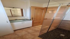 Un baño con cabina de ducha de vidrio, una puerta de madera y un lavabo blanco con un espejo encima.