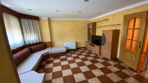 Una habitación con piso a cuadros, un sofá, una mesita, un televisor y un armario.