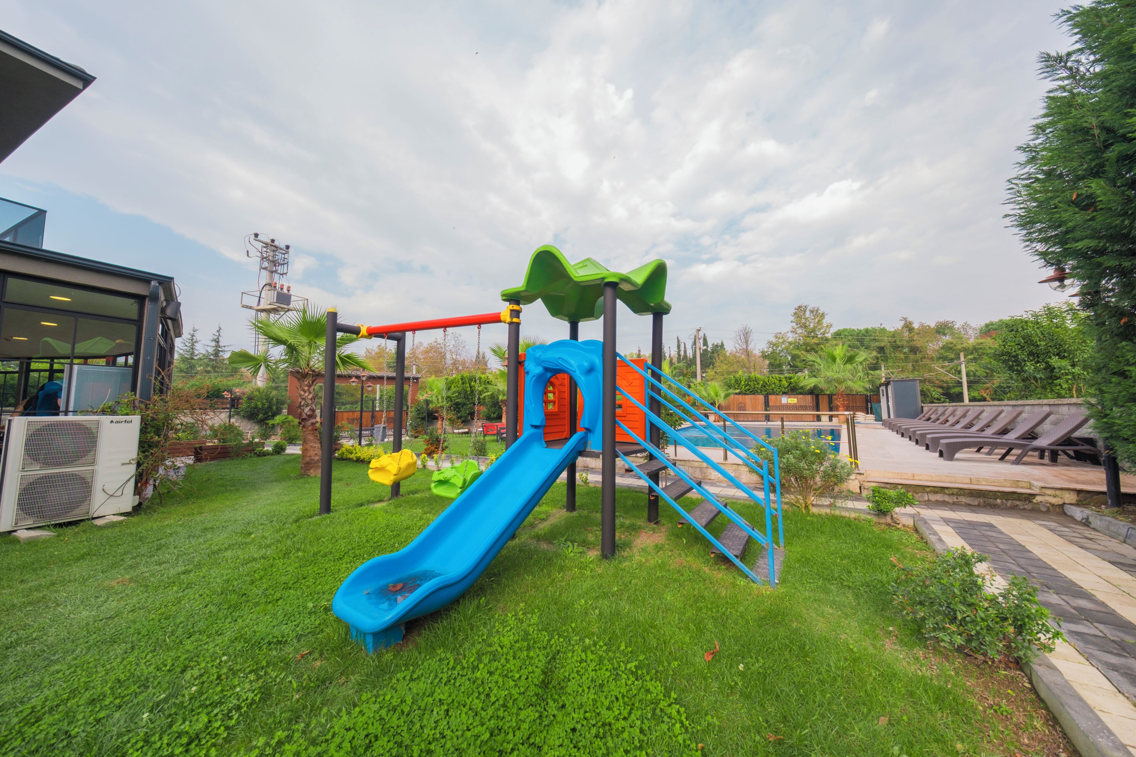 A playground with a blue slide, a red climbing structure, and a green climbing net.