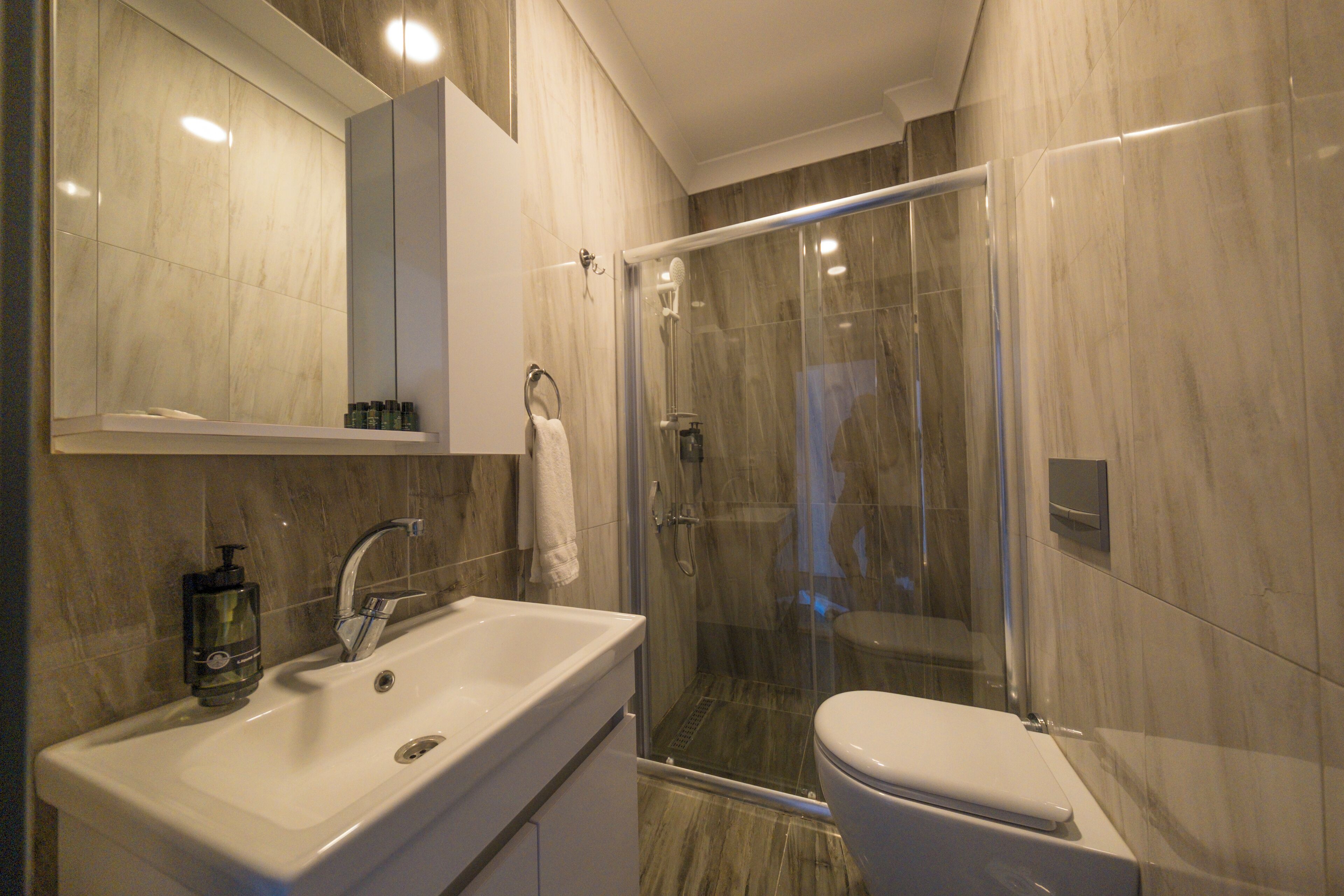 A modern bathroom with a glass-enclosed shower, a white sink with a soap dispenser, and a toilet.