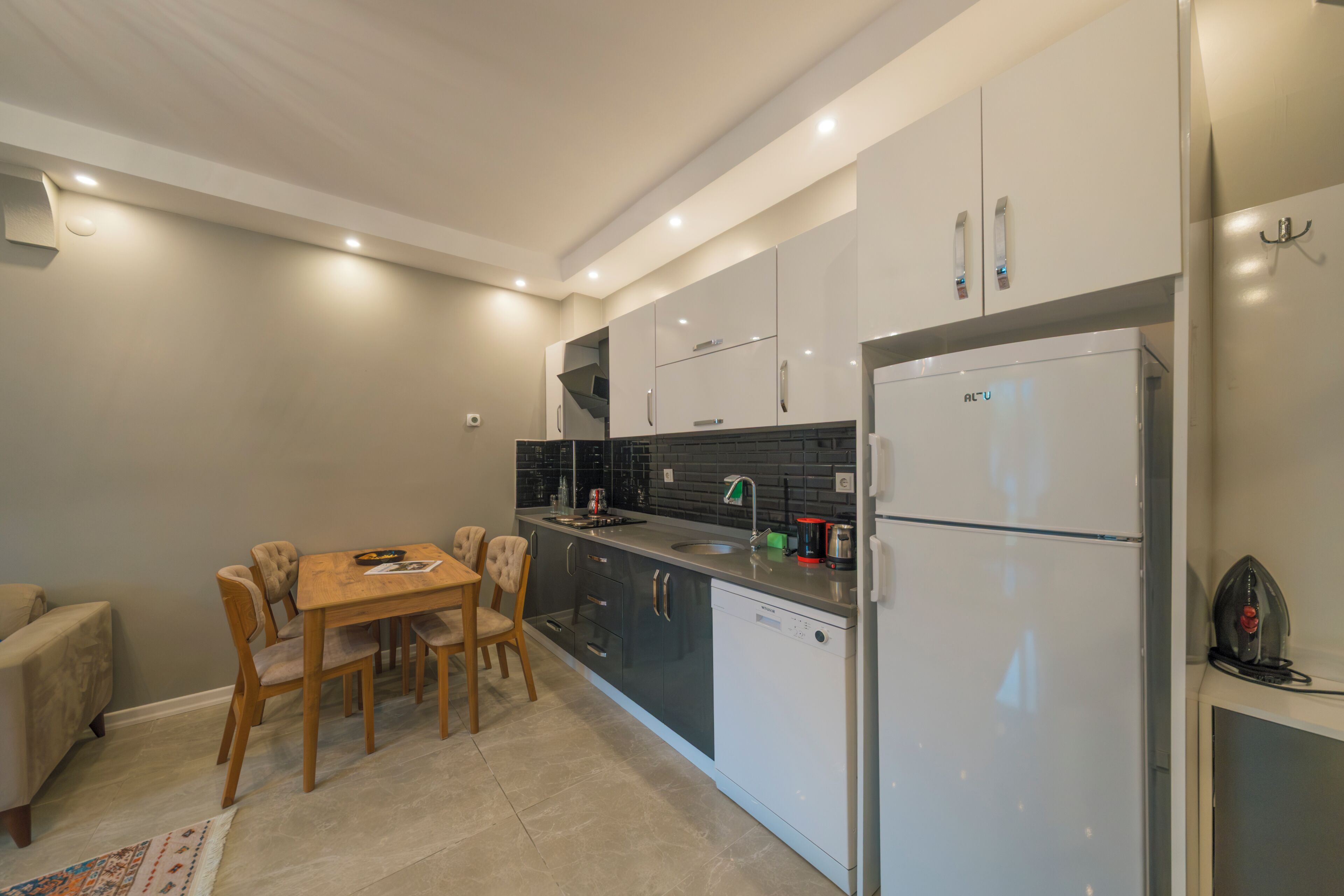 A modern kitchen with a dining area, featuring a built-in dishwasher, a refrigerator, and a black tiled backsplash.