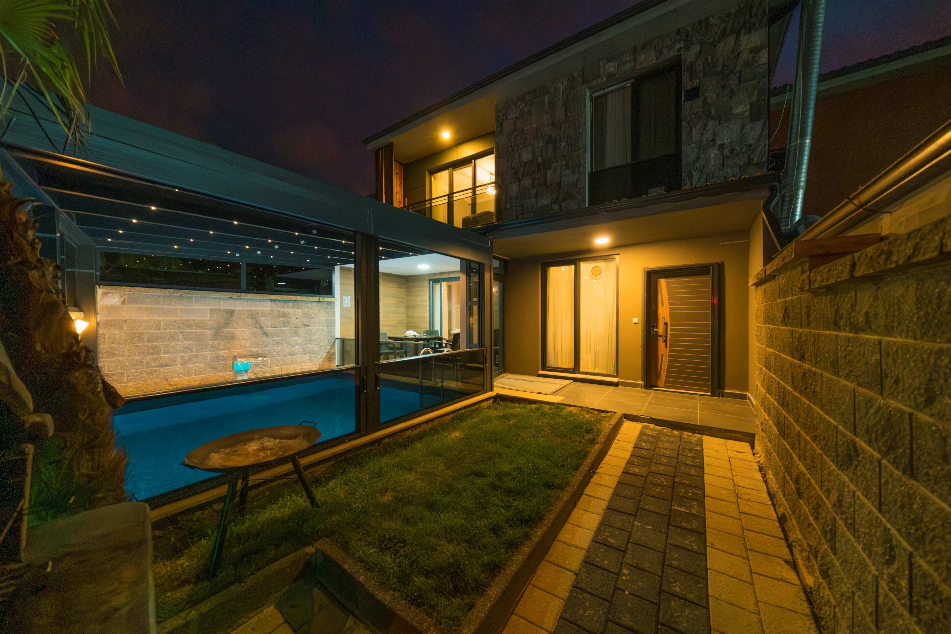 Una casa moderna con piscina, un patio cubierto y un muro de piedra.
