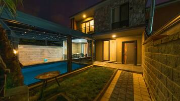 Una casa moderna con piscina, un patio cubierto y un muro de piedra.