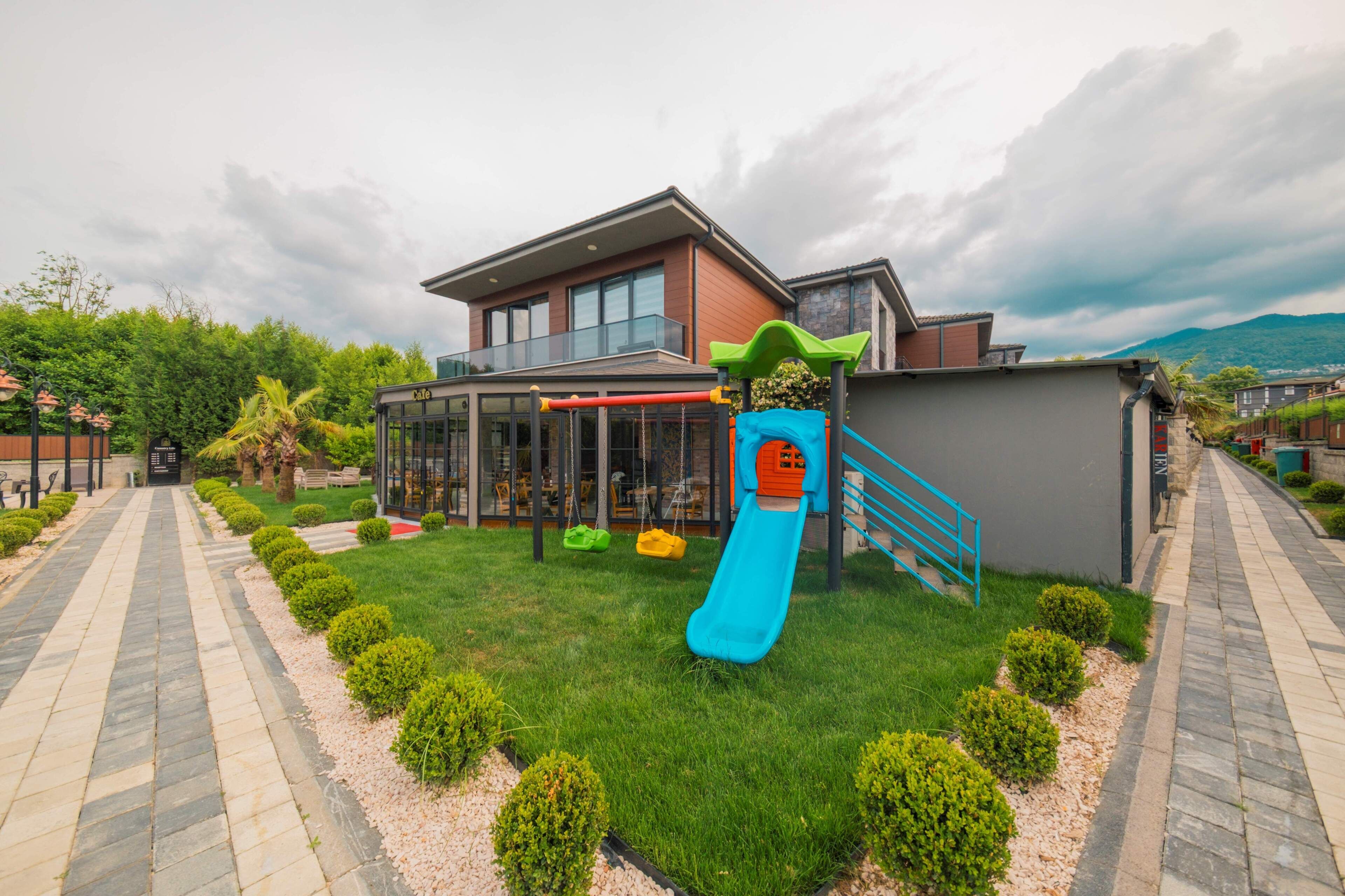 A residential property with a modern house, a children's play area with a slide, a pathway, and a view of a mountain.