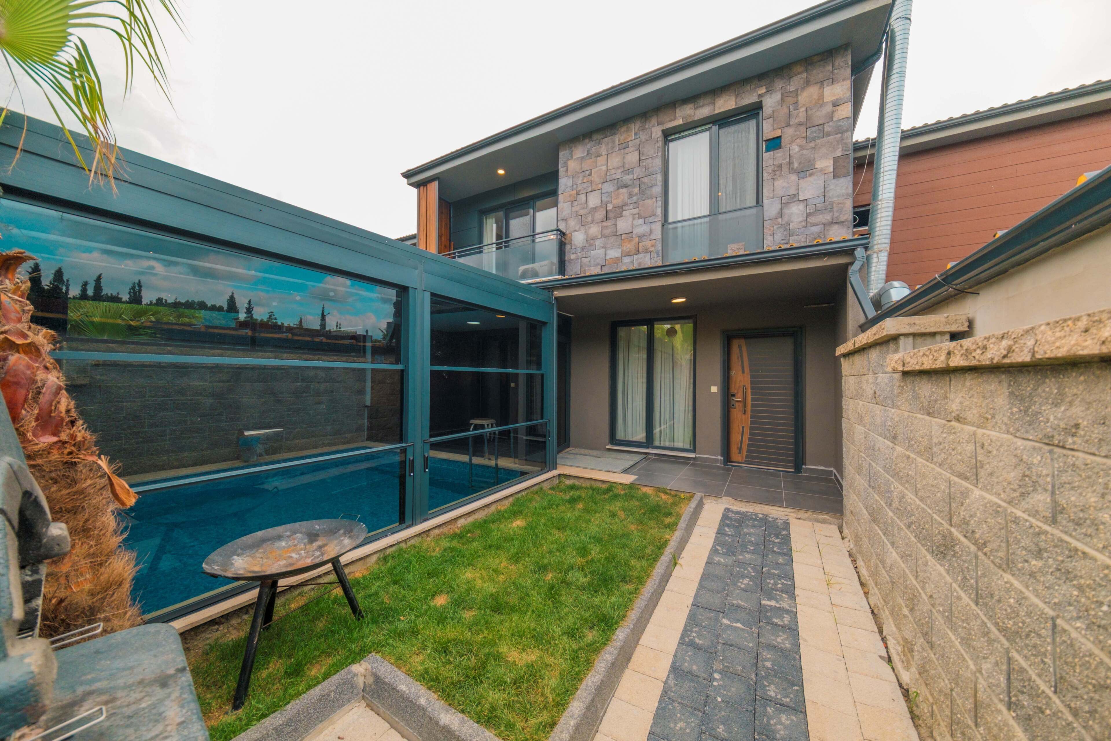A modern house with a swimming pool, a glass-enclosed patio, and a stone facade.