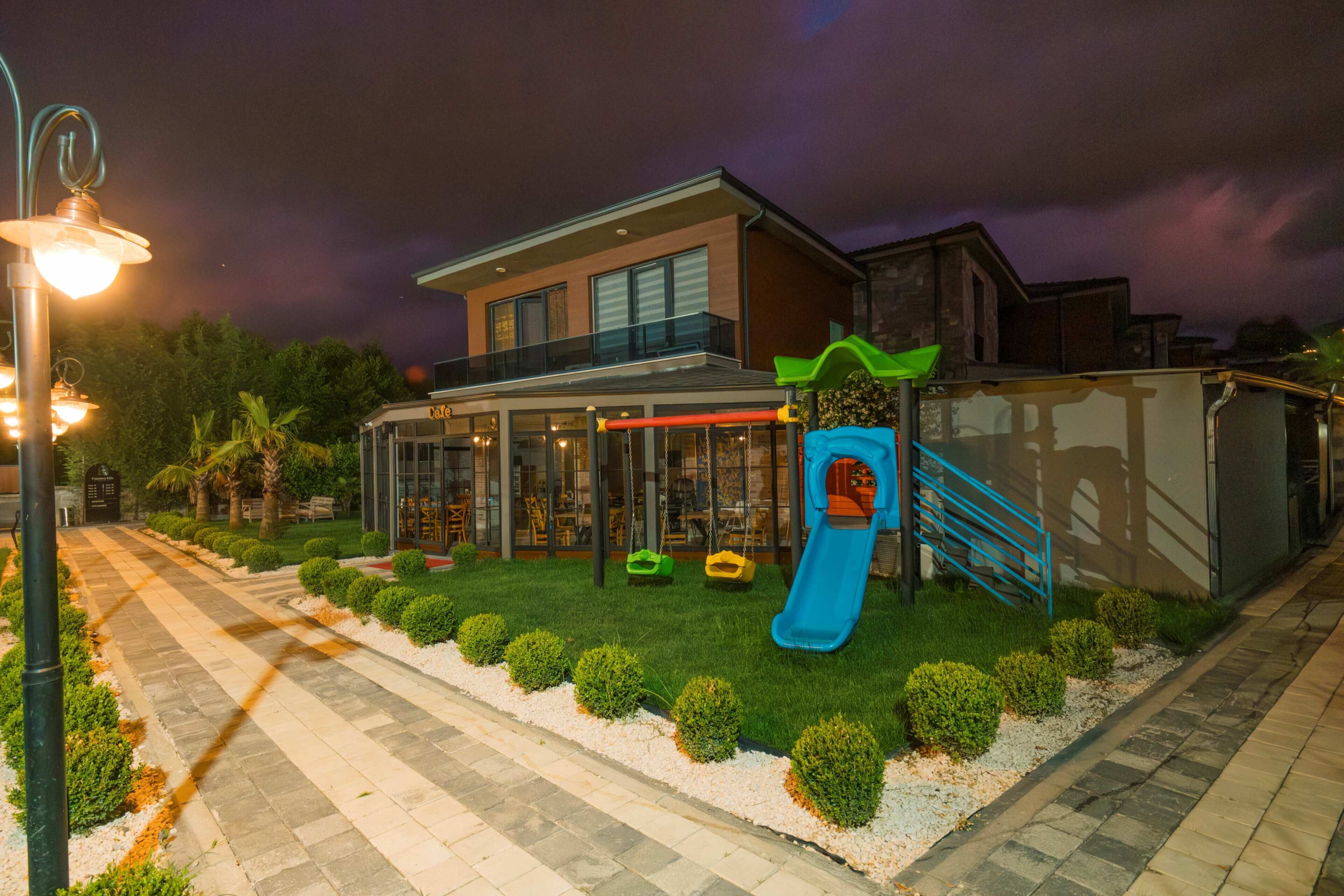 A modern building with a covered patio, a children's play area with a slide, and a well-maintained garden.