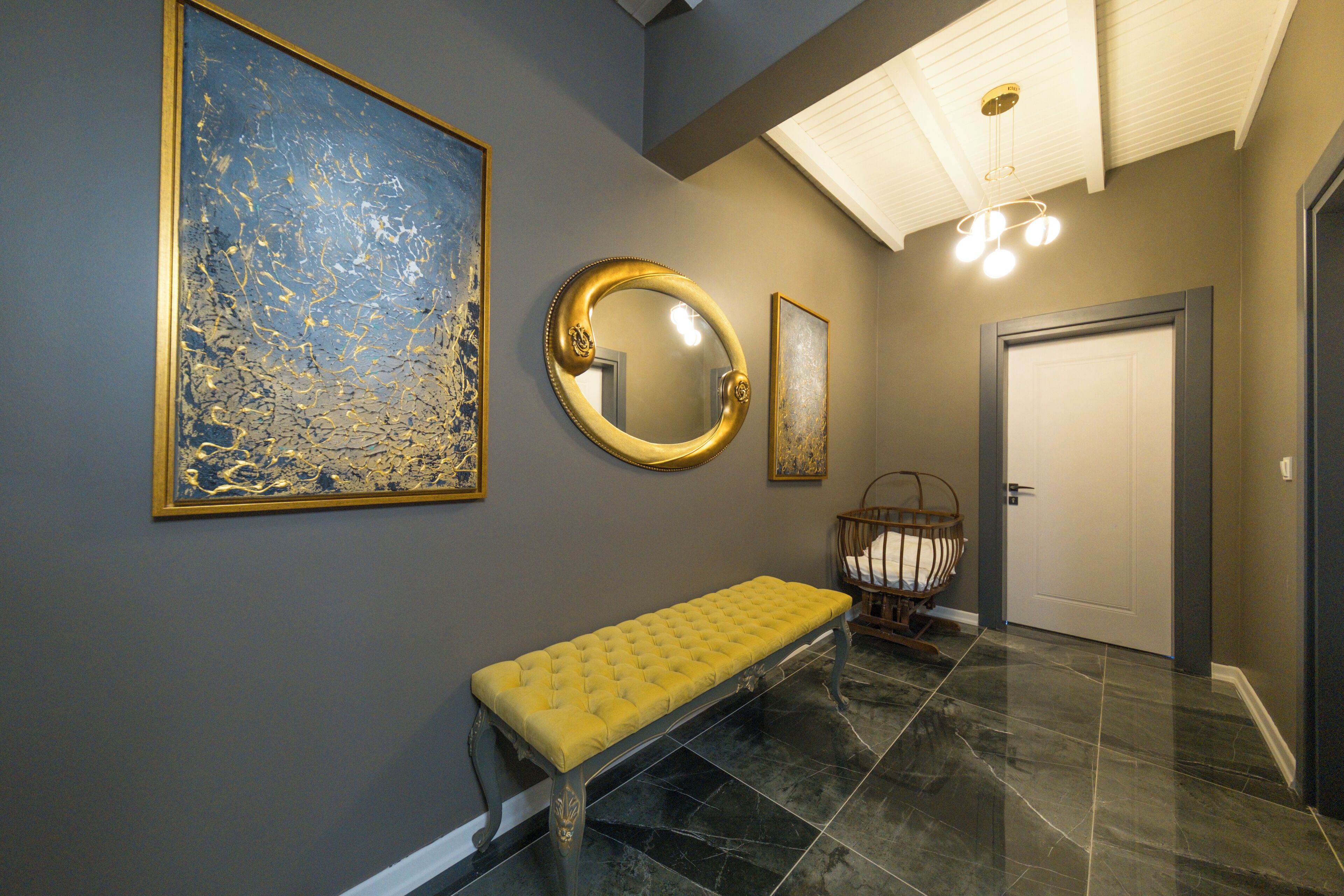 A hallway with a bench, a large abstract painting, a round mirror, and a door.