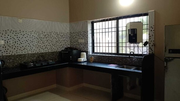 A kitchen with a tiled backsplash, a gas stove, a sink, and a window with bars. - 4-bedroom villa in Karwar with AC (Karwar)
