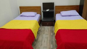 A room with two beds, each with a red and yellow bedspread, a wooden headboard, and a small black nightstand with a phone. - 4-bedroom villa in Karwar with AC (Karwar)