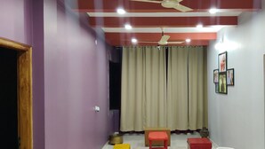 A room with purple walls, a ceiling fan, a window with curtains, and a small table with a chair. - 4-bedroom villa in Karwar with AC (Karwar)