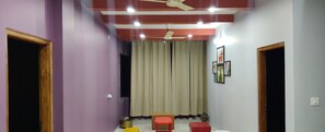A room with purple walls, a ceiling fan, a window with curtains, and a small table with a chair. - 4-bedroom villa in Karwar with AC (Karwar)