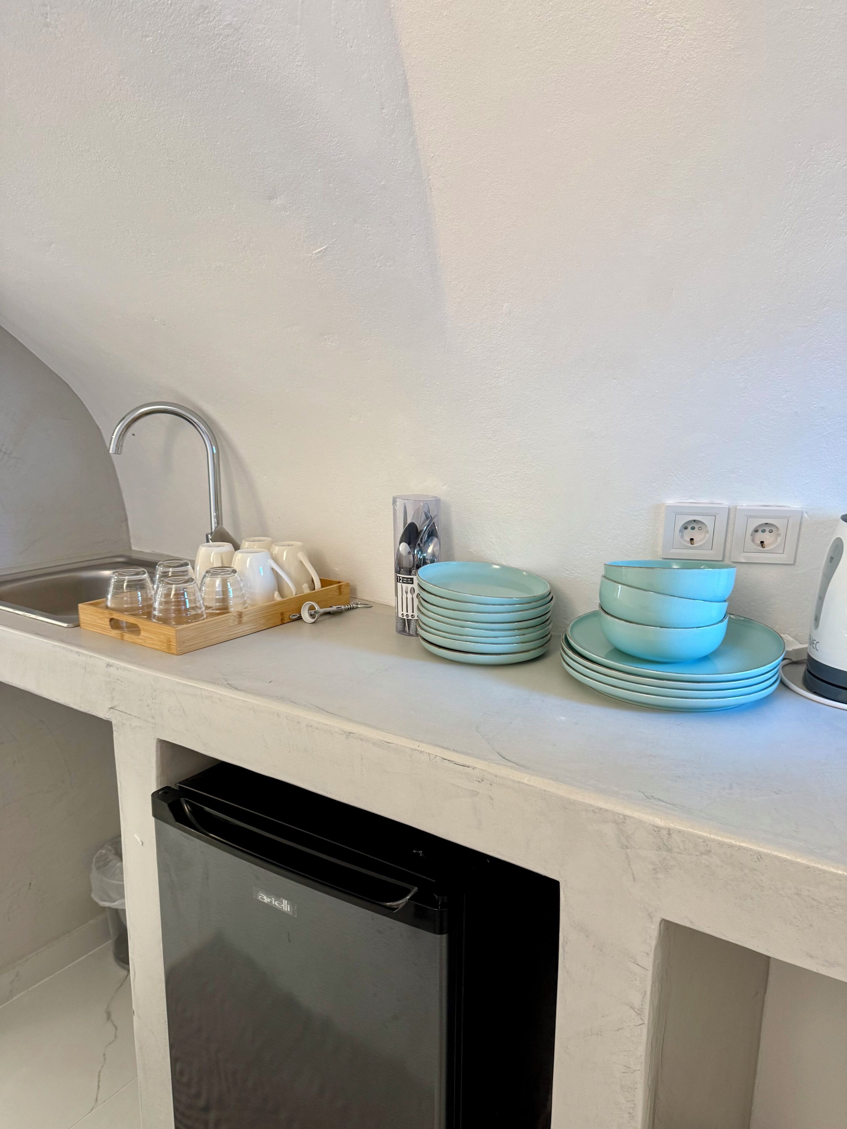 Una cucina con lavello, lavastoviglie e un piano di lavoro con piatti e bicchieri impilati.