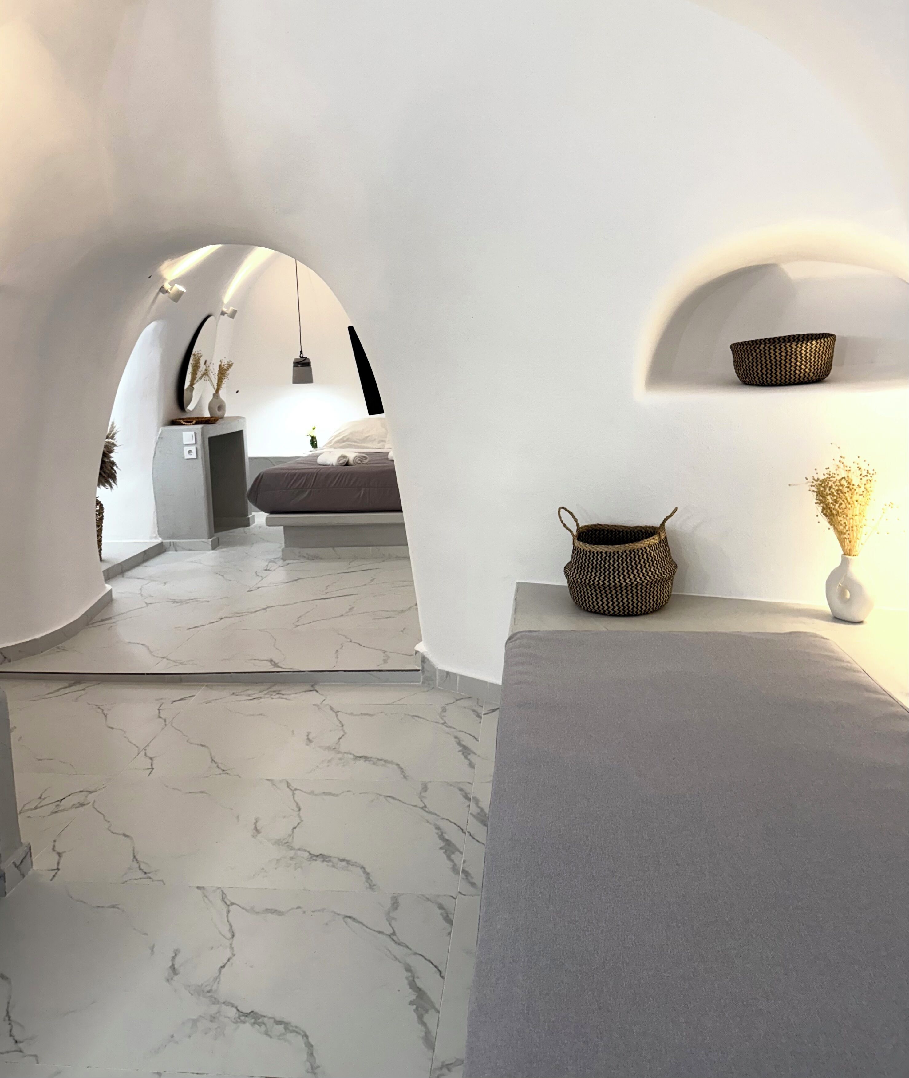 A modern interior with a marble floor, a bed with a gray mattress, and a small table with a woven basket and a vase.
