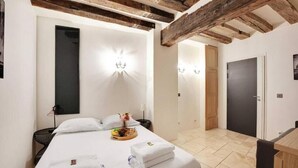 A hotel room with a bed, a bedside table, a tray with toiletries, and a wooden ceiling beam. - Family Apartment - Quartier Latin (Paris)