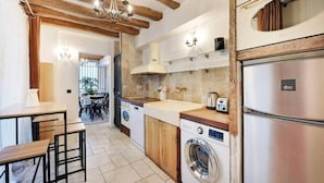 A compact kitchen with wooden beams, a washing machine, a refrigerator, and a dining area with a table and chairs. - Family Apartment - Quartier Latin (Paris)